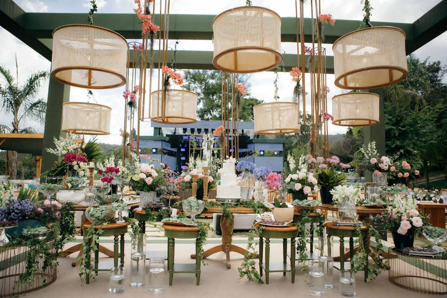 Elegant wedding reception with rattan pendant lights, lush floral arrangements, and a beautifully decorated dessert table.