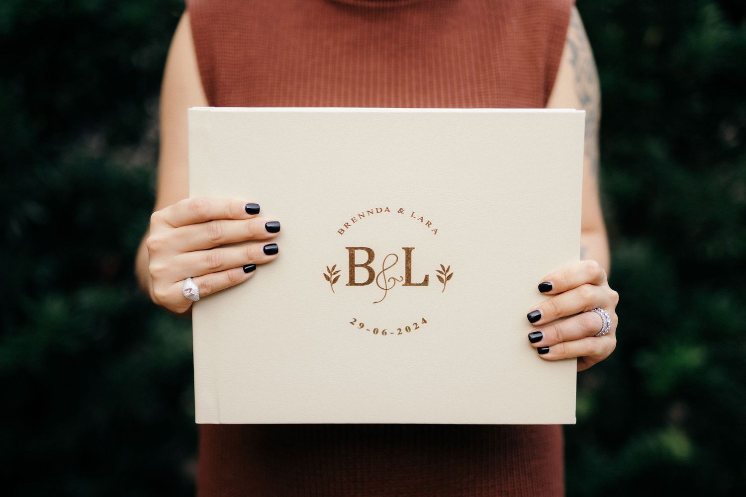 Person holding a cream wedding guest book with gold monogram B&L initials and floral design, dated 25-06-2024.