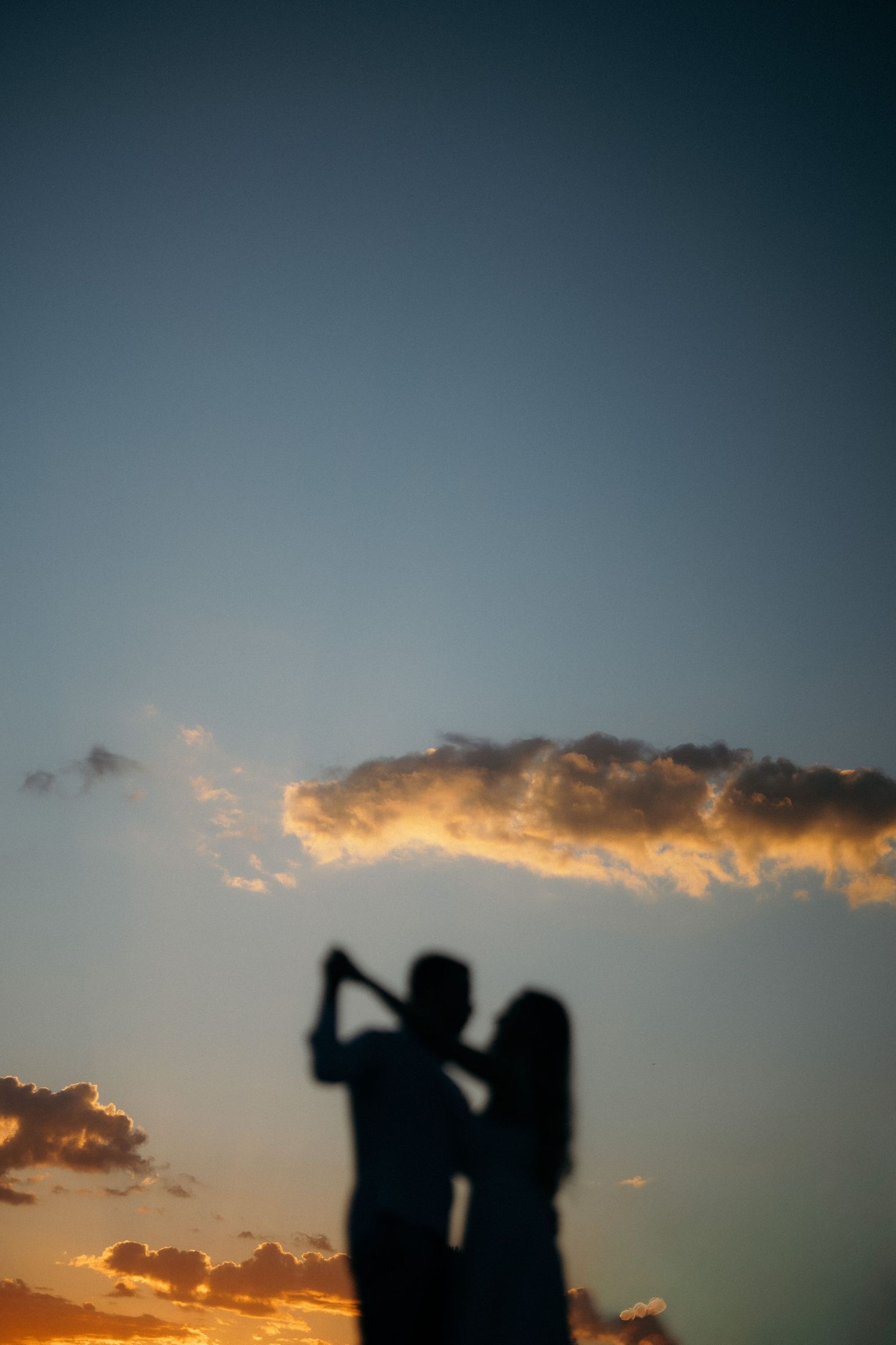 Silhouette of a couple dancing against a vibrant sunset sky with dramatic clouds and warm orange hues.