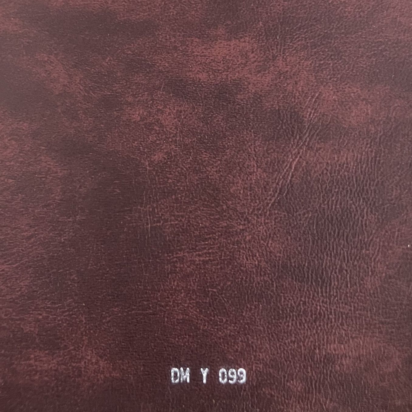 Close-up of deep burgundy distressed leather texture fabric swatch labeled DM Y 099.