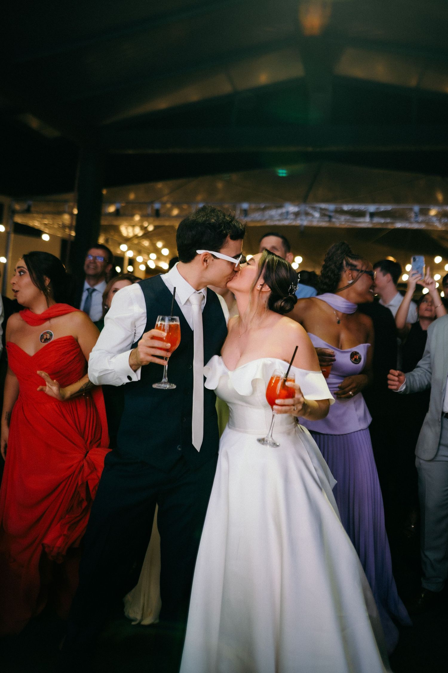 Bride and groom sharing a kiss on the dance floor holding cocktails at their wedding reception.