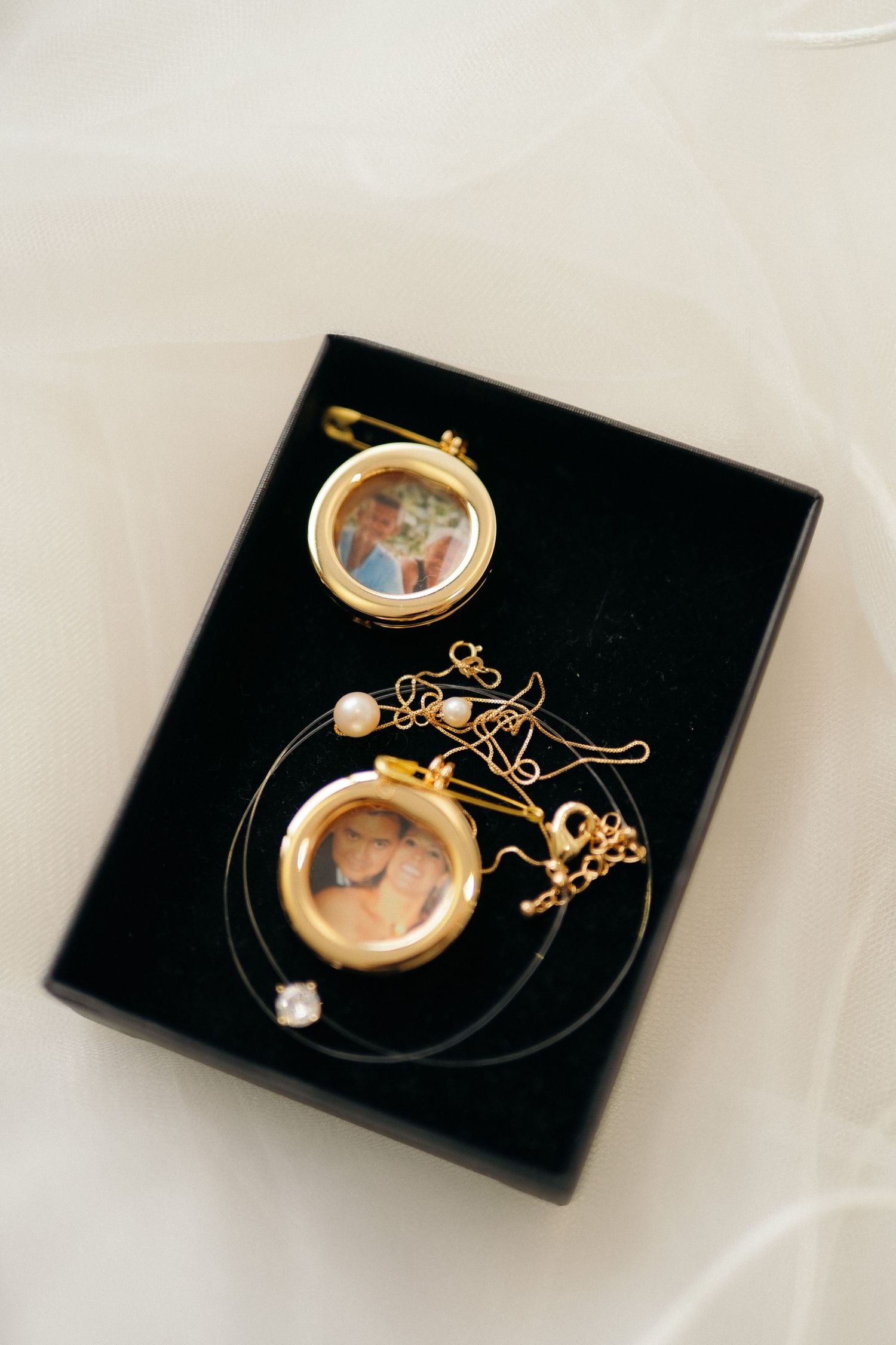 Gold locket pendants with photos inside displayed in a black jewelry box with delicate chain necklaces.