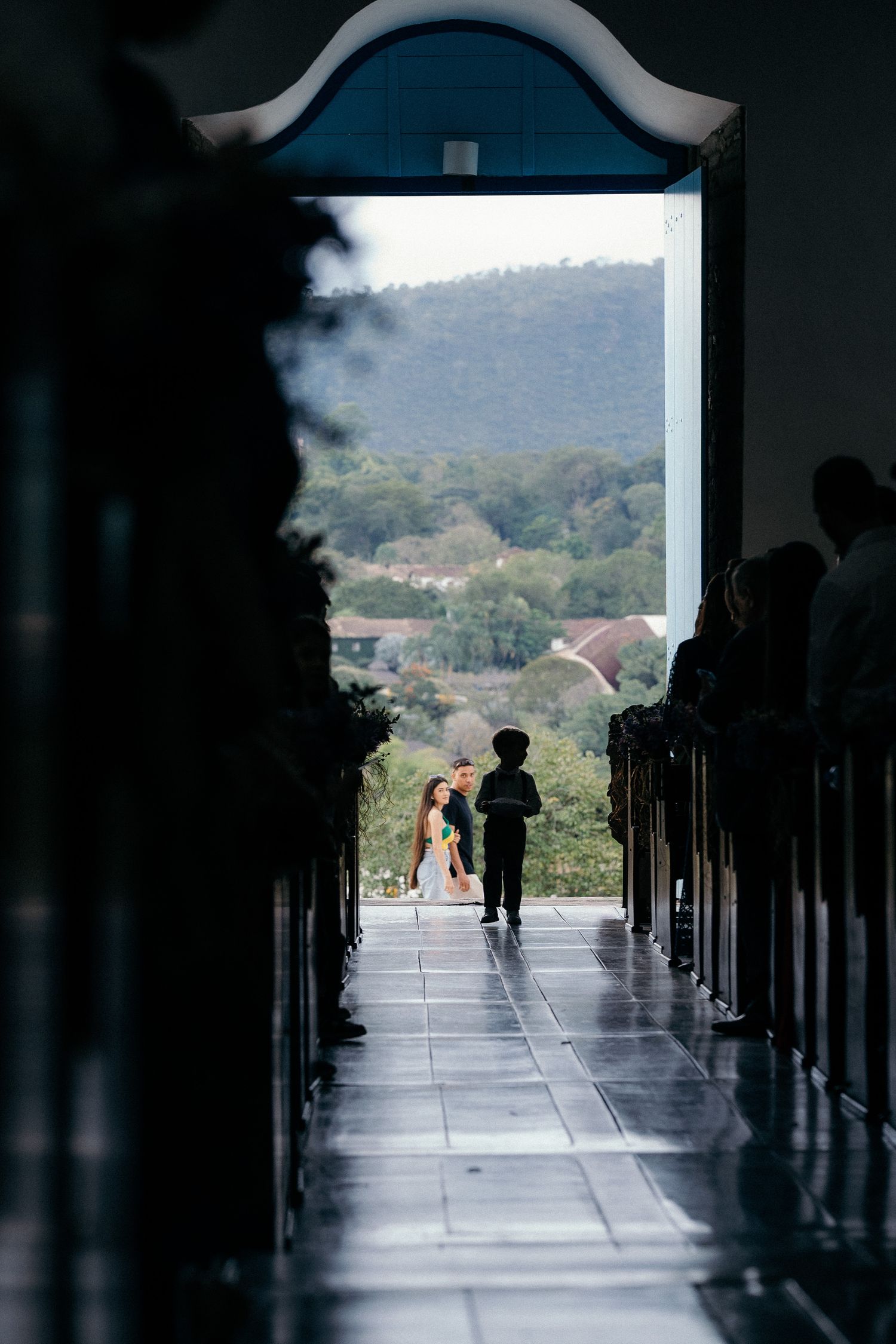 Silhouette of wedding couple at church altar with mountain landscape view through open doors.