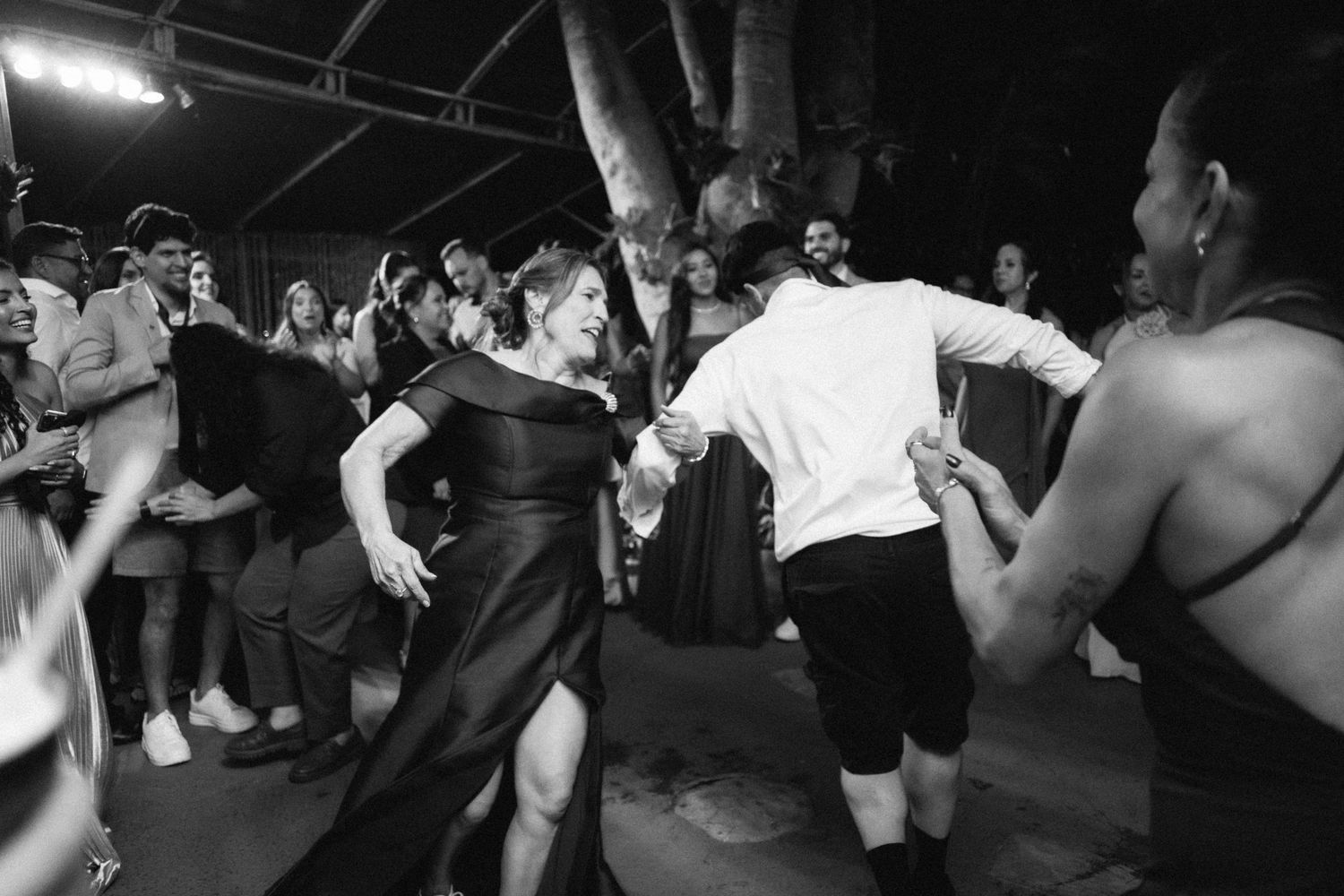 Black and white photo of guests dancing energetically at lively outdoor wedding reception party.