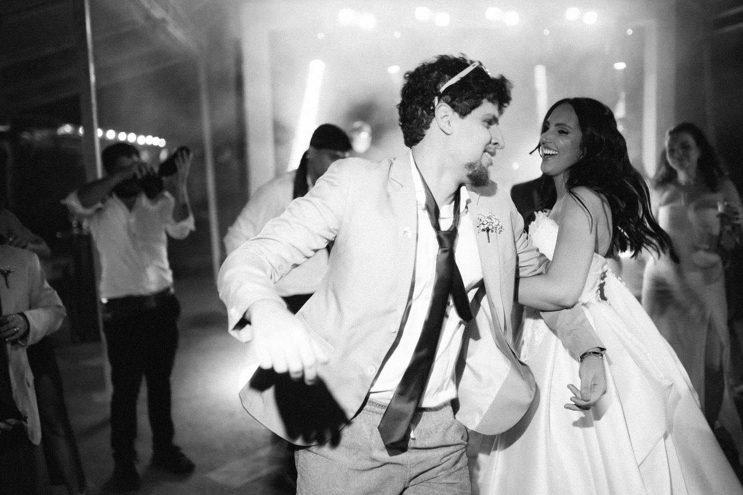 Bride and groom dancing joyfully together at wedding reception in black and white photo.