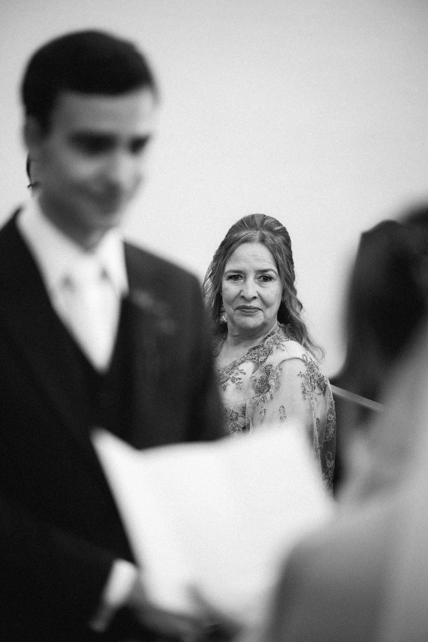 Black and white photo of a woman watching intently during a wedding ceremony while couple exchanges vows.
