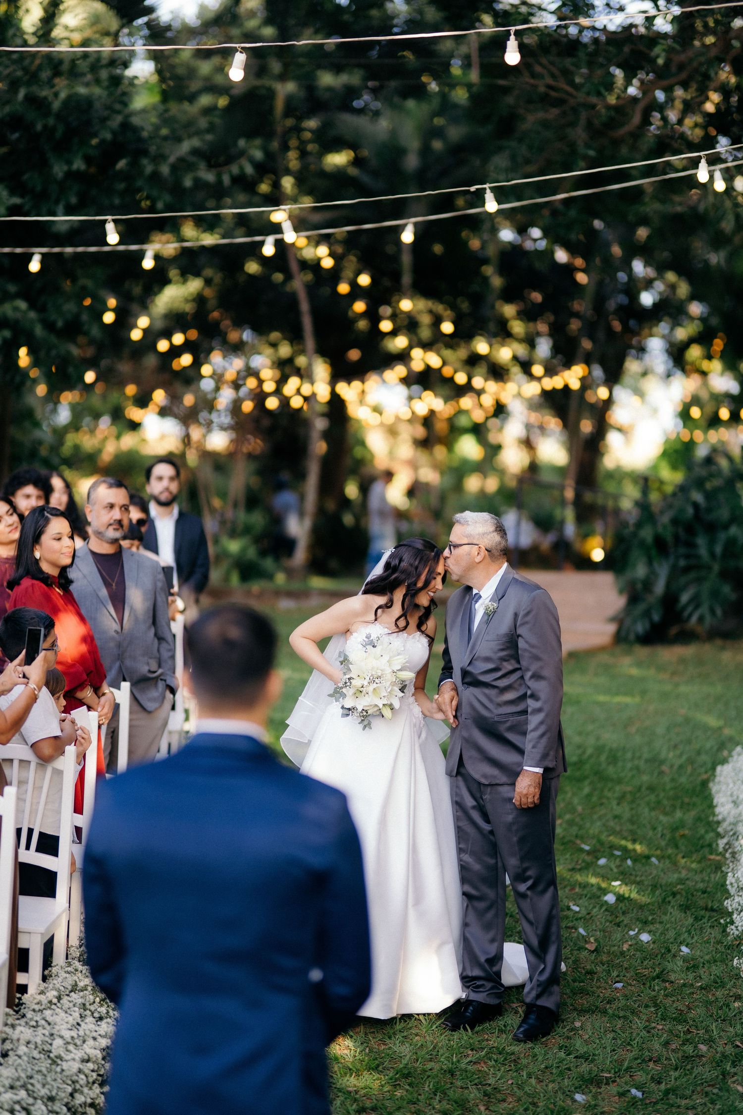 Father of the bride sharing a kiss with daughter during outdoor garden wedding ceremony.