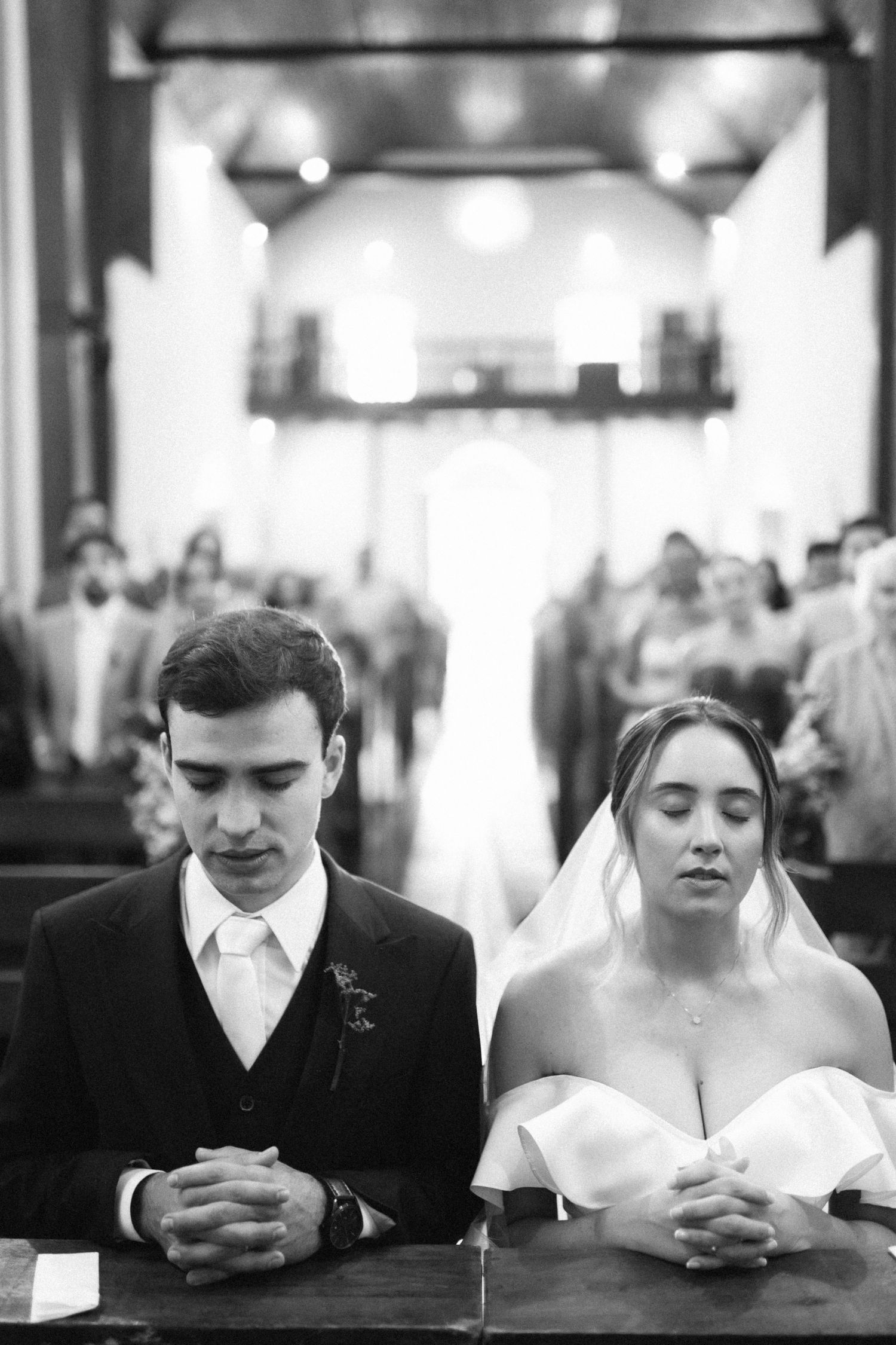 Black and white photo of bride and groom praying together at church altar during wedding ceremony.