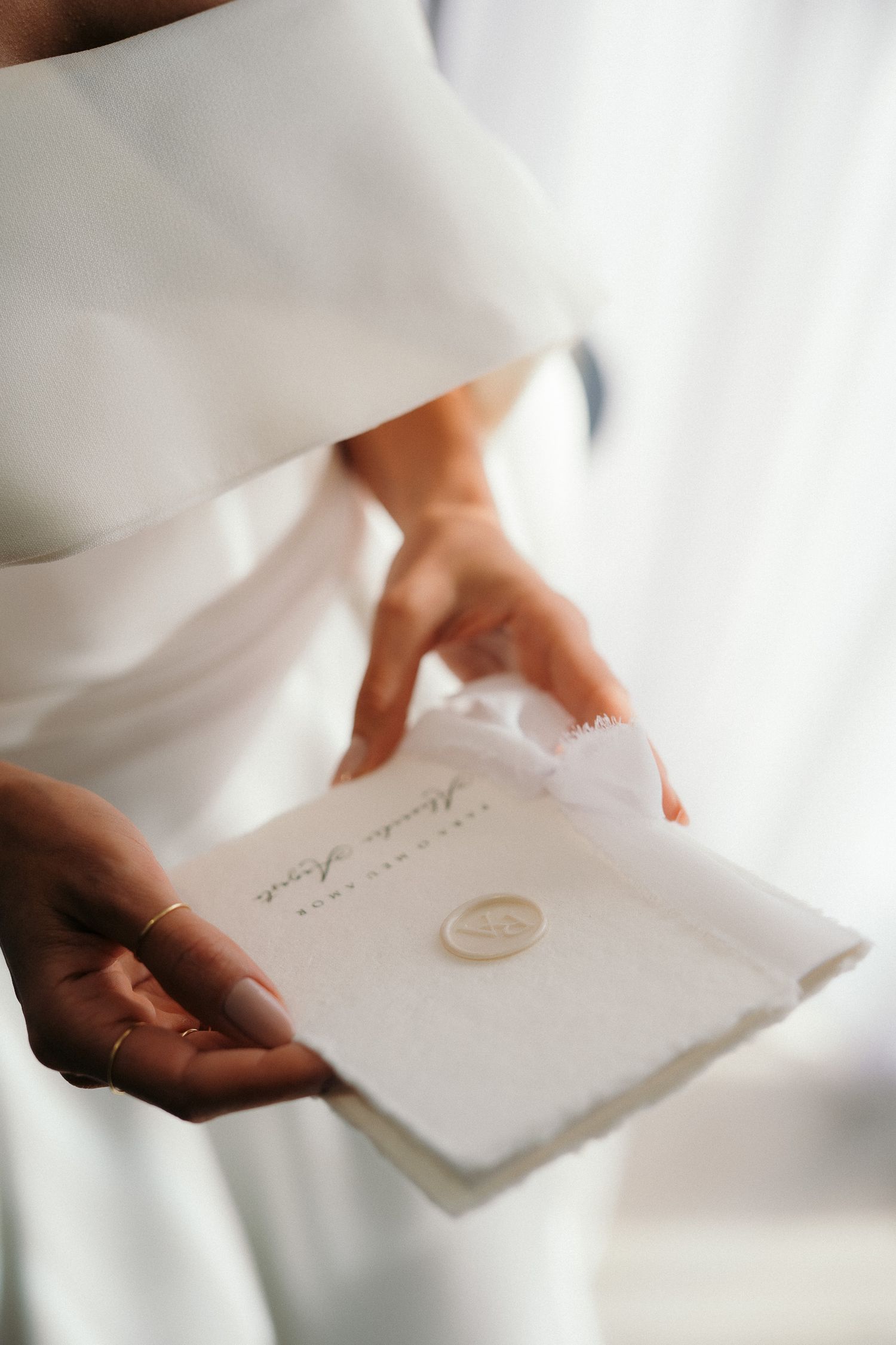 Bride holding an elegant white wedding invitation with gold wax seal in delicate hands.