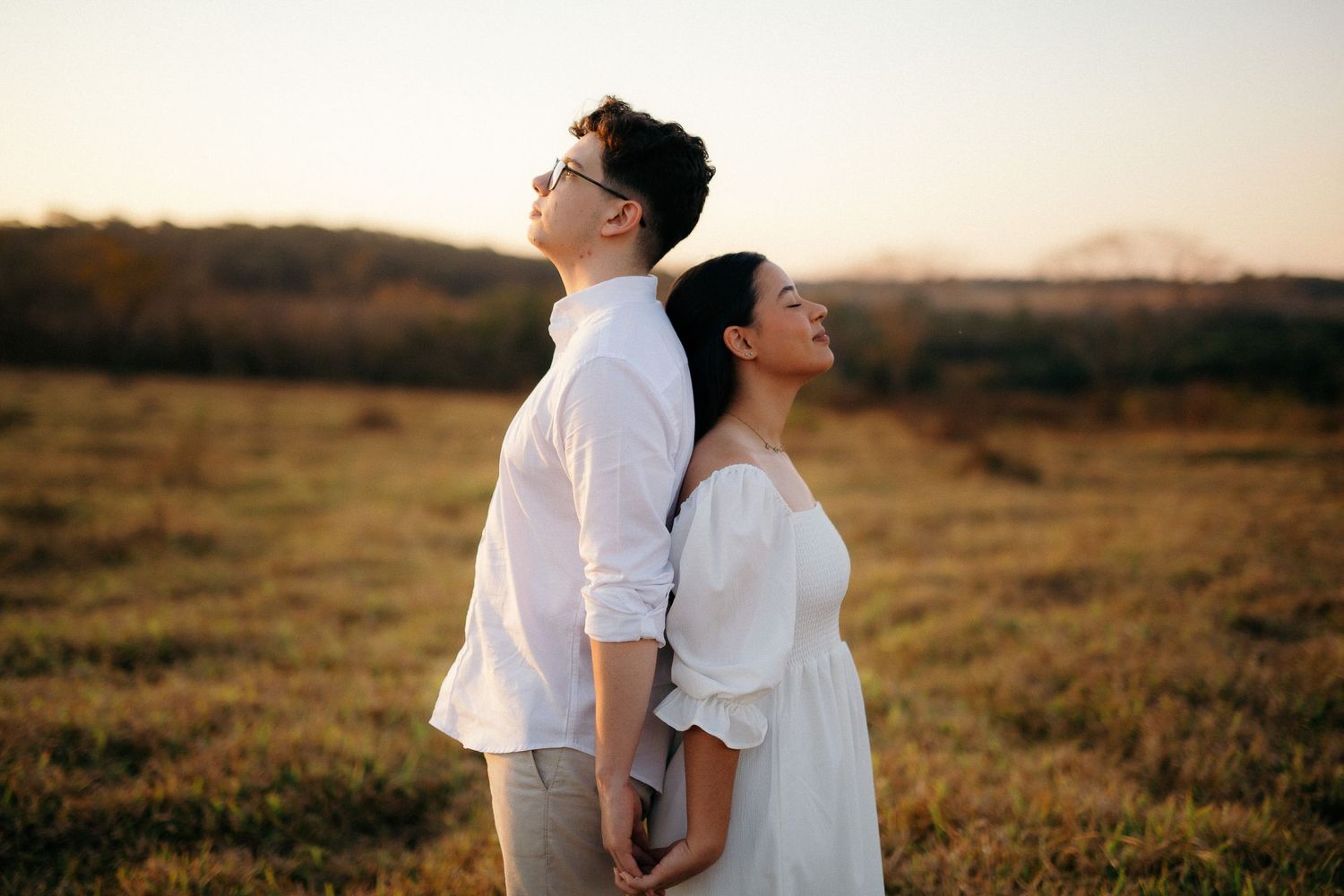 Couple standing back to back with eyes closed in a golden sunset field.