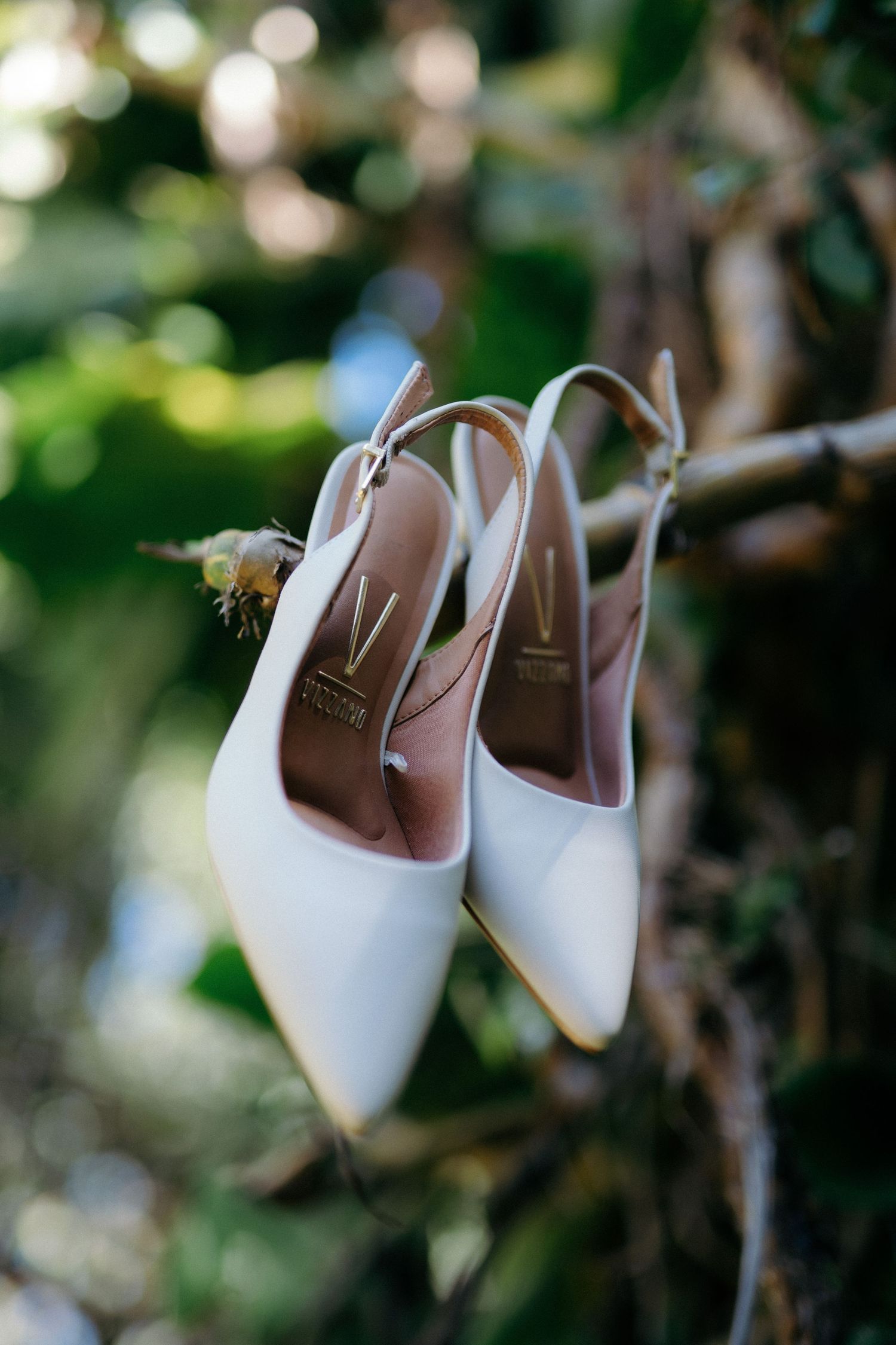 White slingback heels hanging on a branch in a garden, perfect bridal wedding shoes.