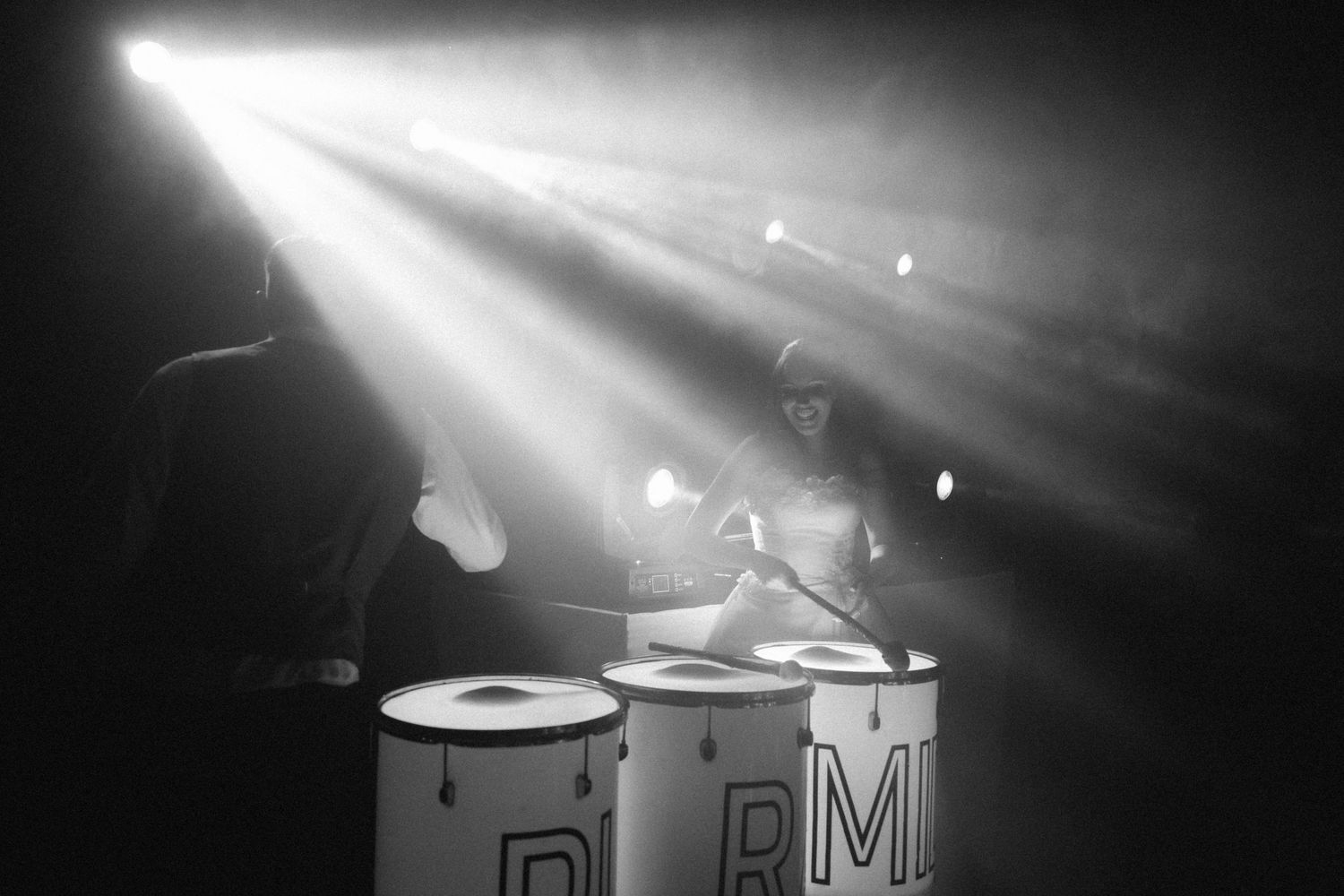 Black and white dramatic shot of drummer performing under spotlight beams at wedding reception.