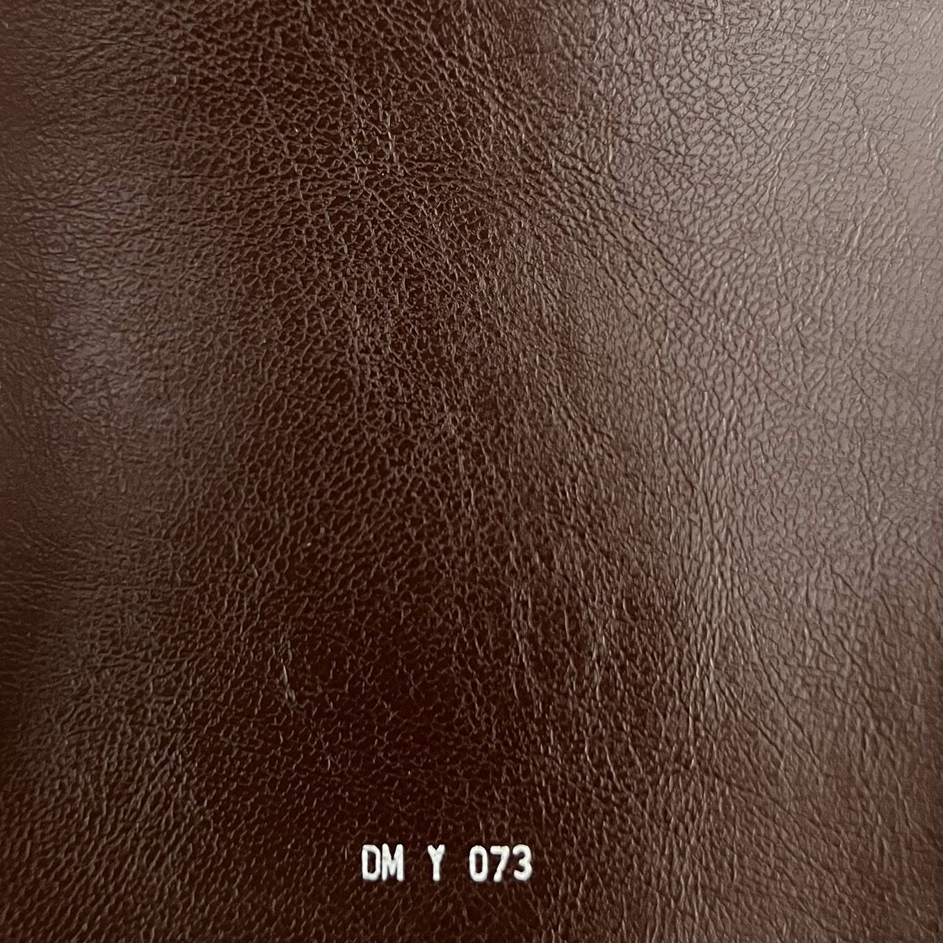 Rich dark brown leather fabric swatch with natural grain texture, labeled DM Y 073.