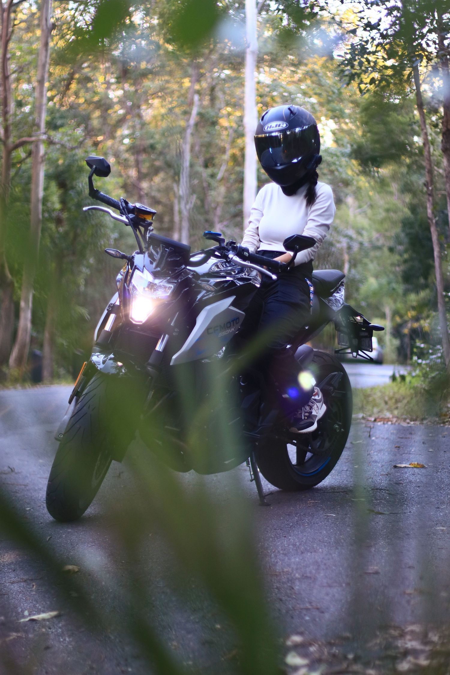 A motorcyclist in a black helmet and white jacket sitting on a modern motorcycle on a forest road.