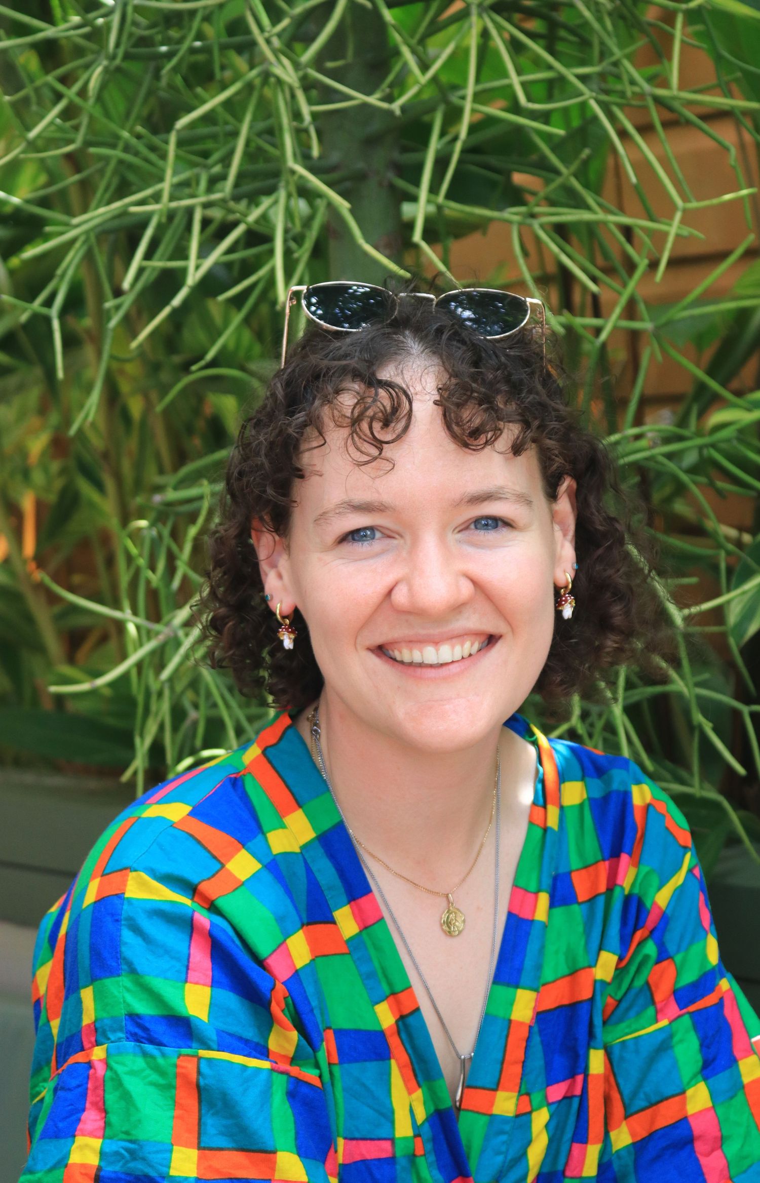 Happy woman with curly hair and sunglasses on head wearing colorful shirt outdoors.