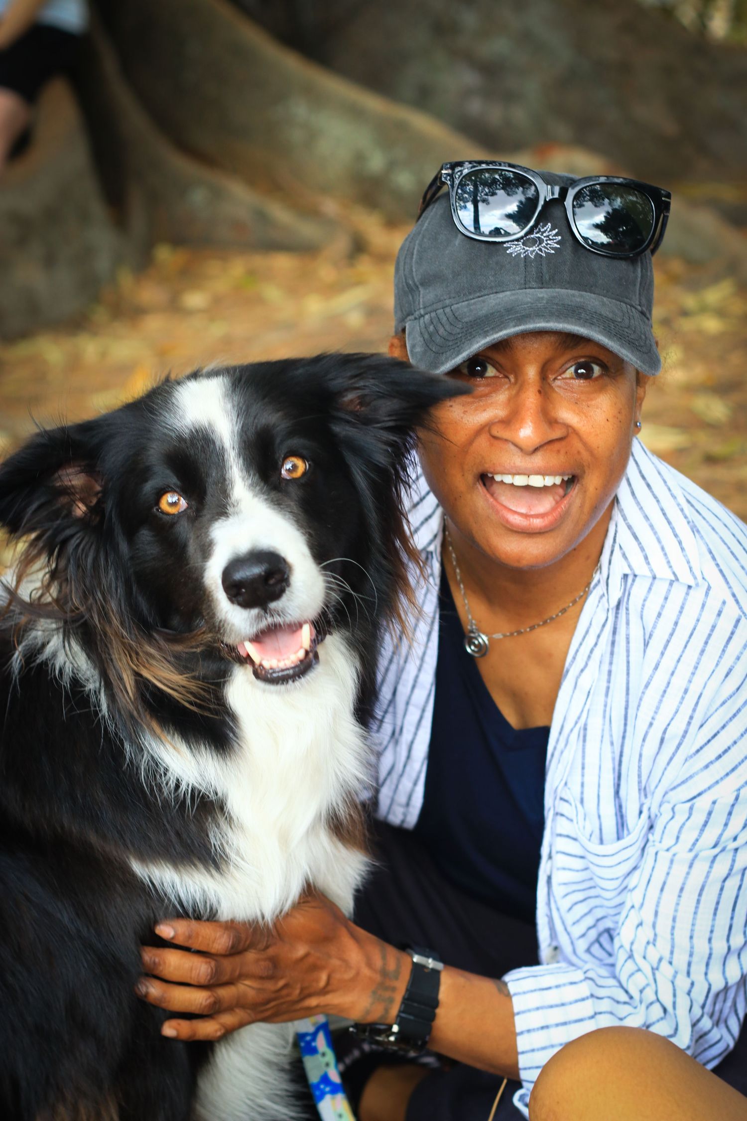Smiling woman in gray cap posing with a black and white Border Collie dog outdoors.