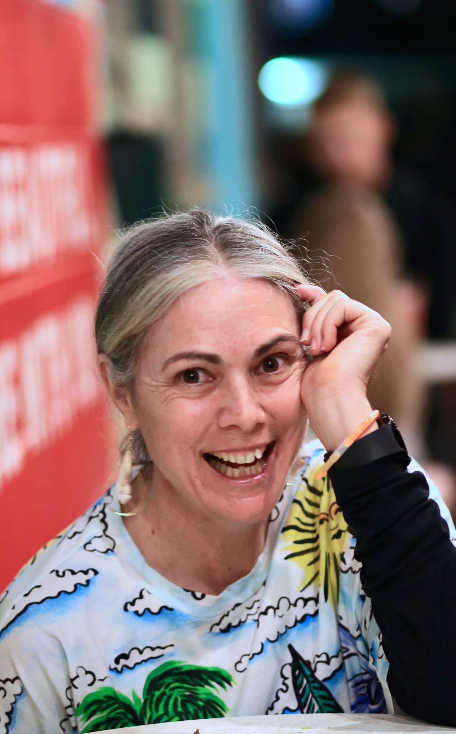 Happy middle-aged woman with gray hair wearing tropical print shirt laughing at outdoor event.