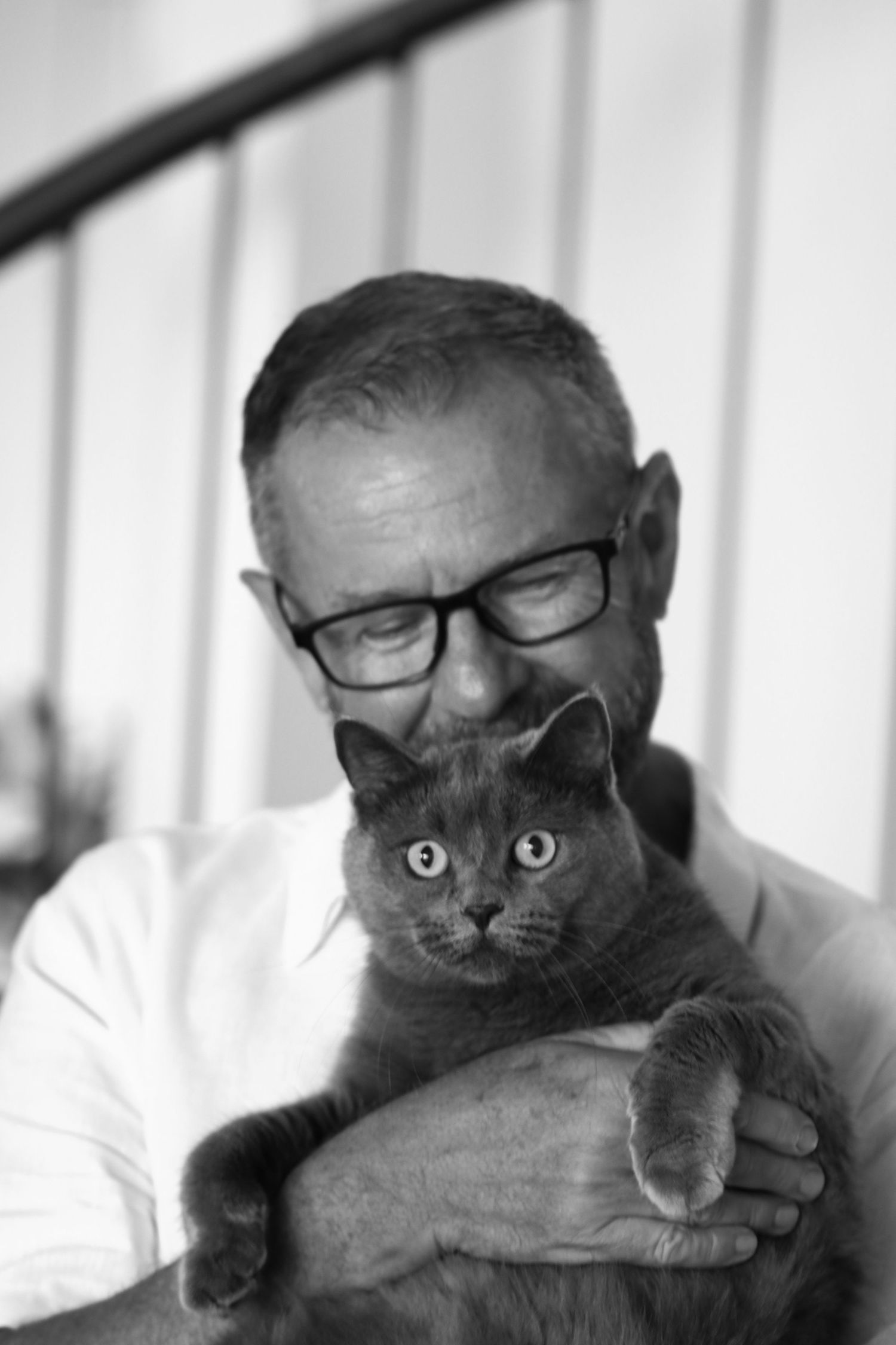 Black and white portrait of a middle-aged man with glasses tenderly holding a fluffy gray cat.