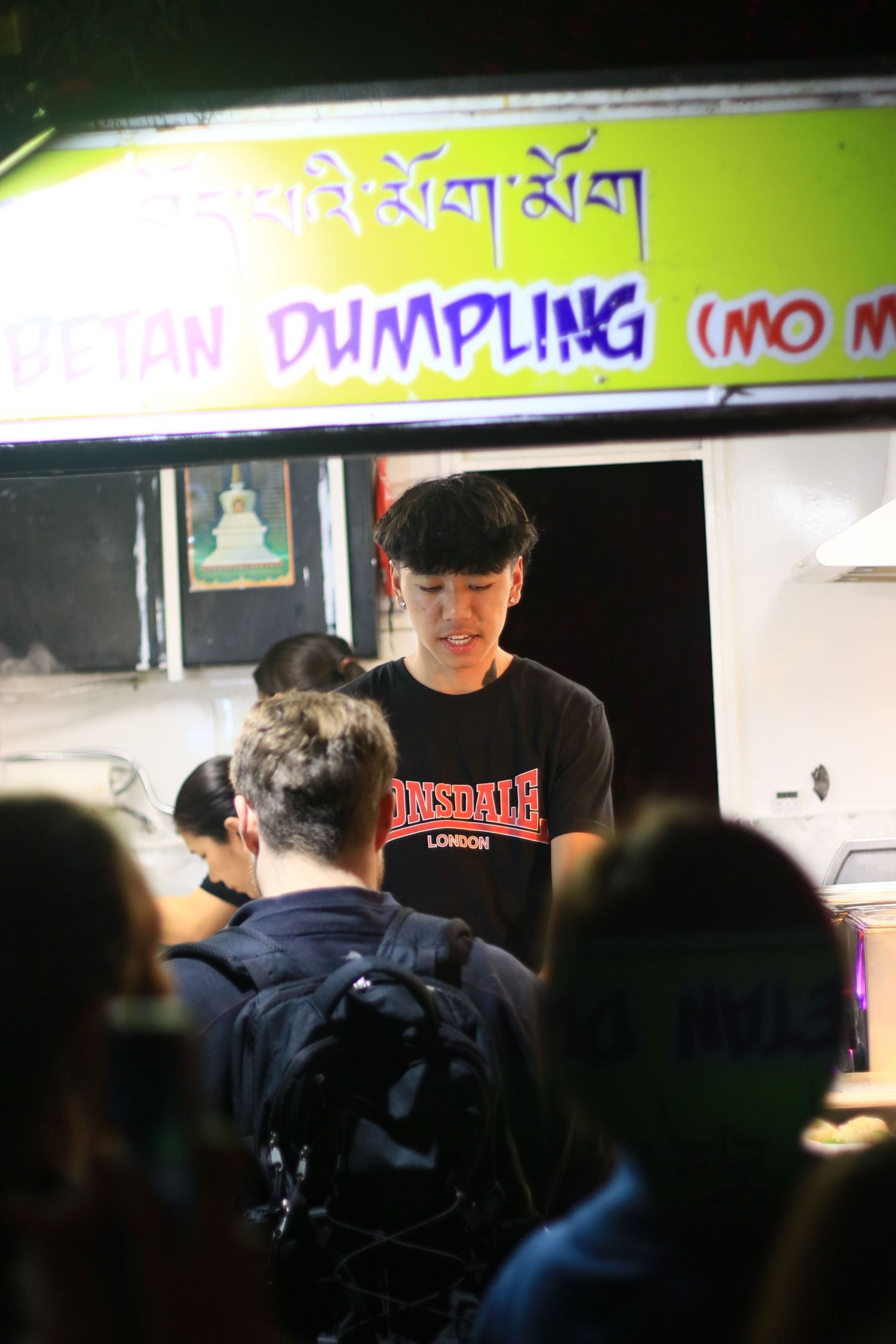 Young man serving customers at a Tibetan Dumpling Mo Mo street food stall at night.