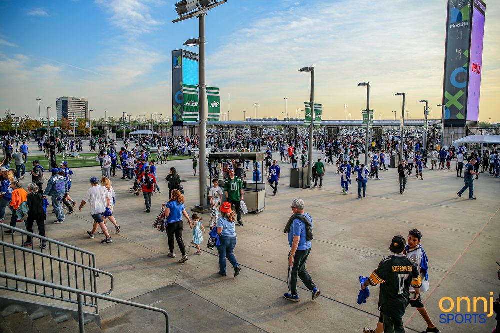 Crowds of NFL fans walk outside MetLife Stadium on a sunny game day evening.