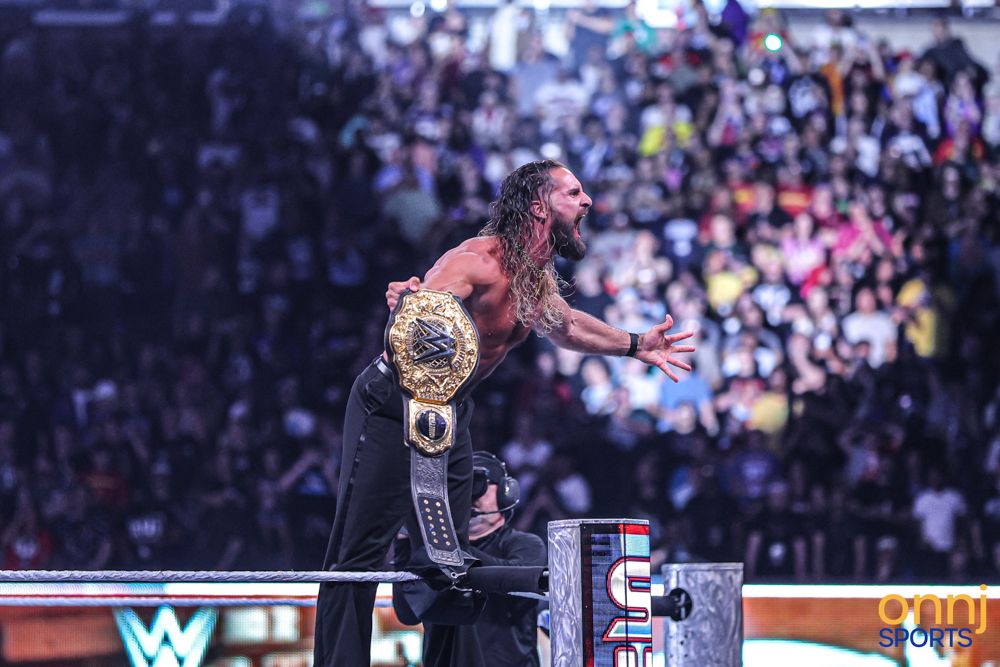 WWE champion raises title belt triumphantly on the ring apron before a massive SummerSlam crowd.