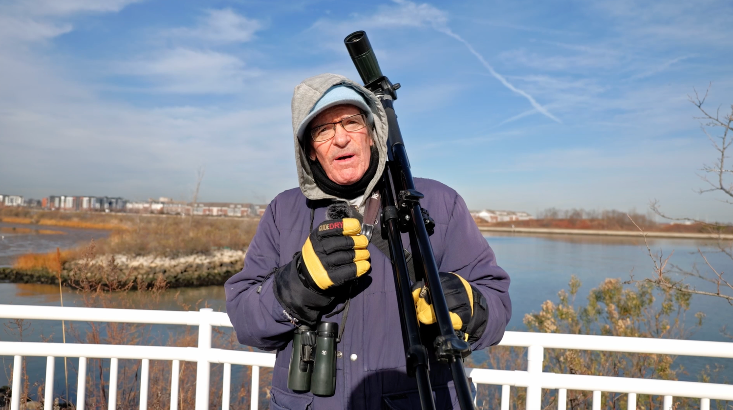 Man with spotting scope on tripod birdwatching at a wetland reserve on a clear winter day.