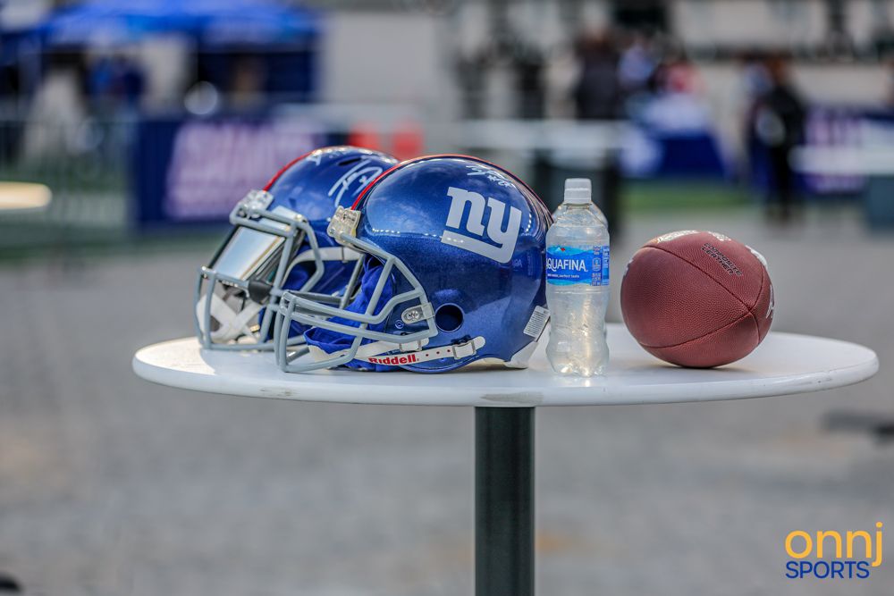 New York Giants NFL helmet and football displayed on a white table at an outdoor fan event.