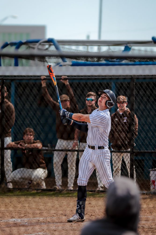 High school baseball player in pinstripe uniform watches ball after powerful swing.