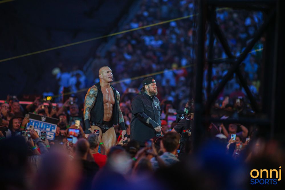 Tattooed WWE superstar walks through crowd at SummerSlam with security escort.