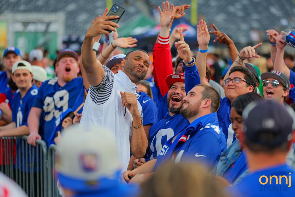New York Giants fans take a group selfie while cheering at an outdoor NFL stadium event.