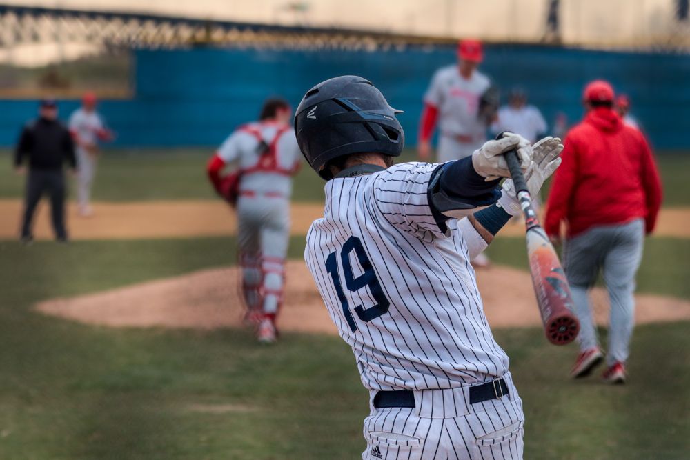 High school baseball batter number 19 in pinstripe uniform prepares to swing at pitch.