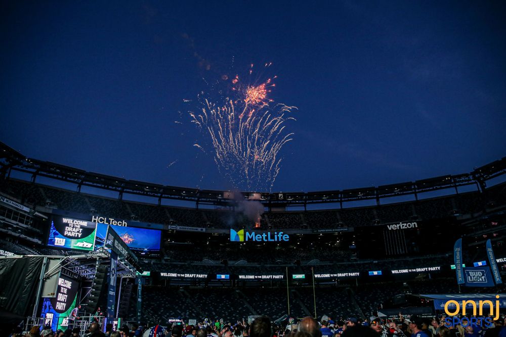 Colorful fireworks explode over MetLife Stadium during a nighttime New York Giants NFL game.
