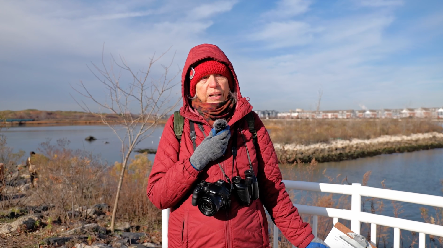 Woman in red winter jacket with camera at a wetland nature reserve on a sunny day.
