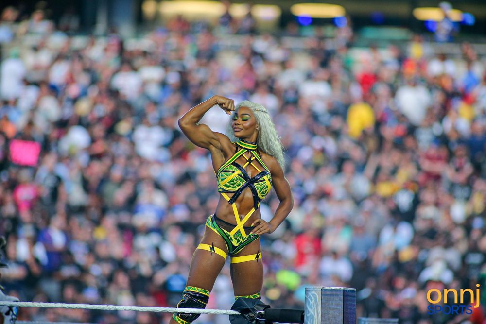 Female WWE wrestler flexes in colorful yellow and green ring gear at SummerSlam before a packed crowd.