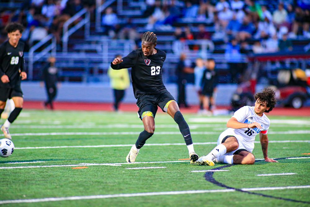 Soccer player in black number 23 jersey dribbling past sliding defender during night match.