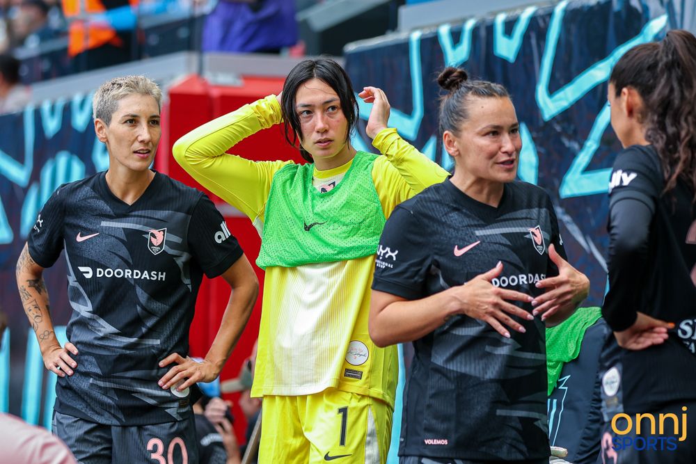 Three female soccer players including a goalkeeper in yellow jersey stand together during NWSL match.