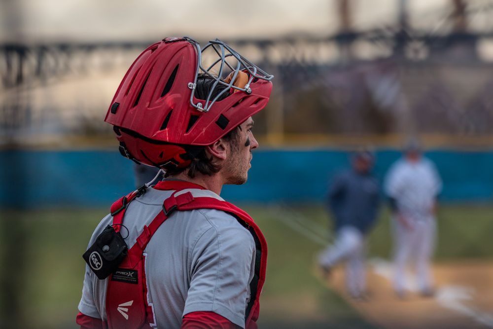 Red-helmeted Easton catcher watches play at home plate during youth baseball game.