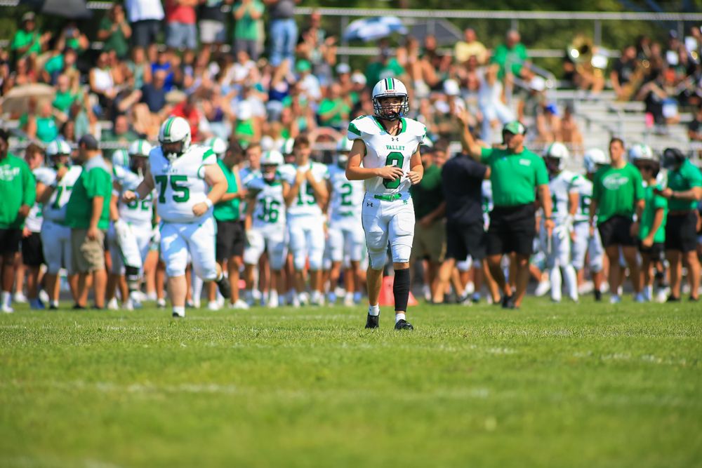 Green and white football players jogging onto field during warm-ups at an outdoor stadium.