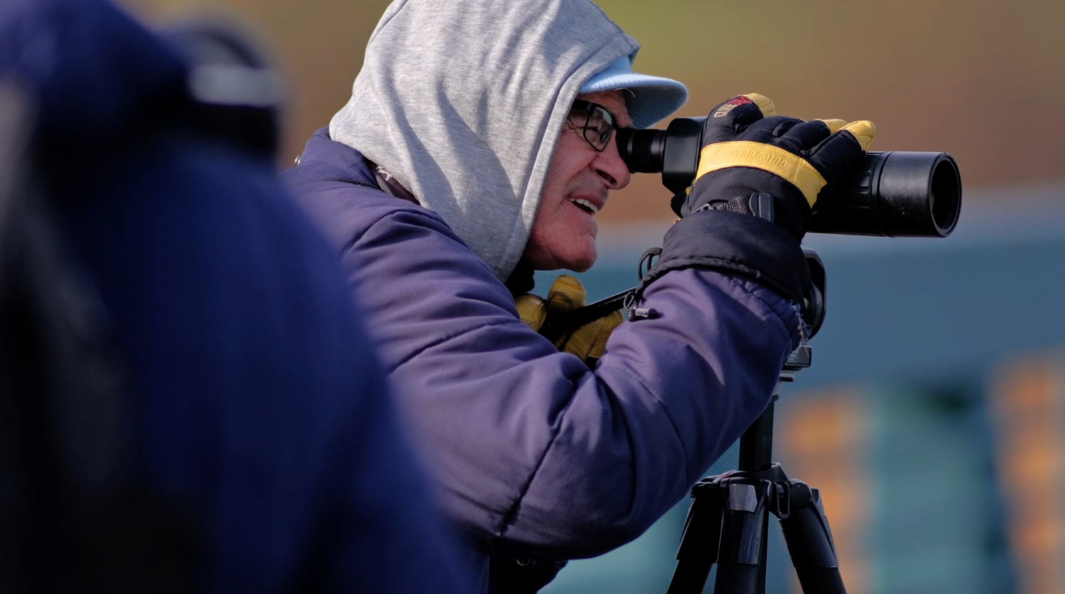A person in a purple hooded jacket photographs wildlife using a camera mounted on a tripod outdoors.