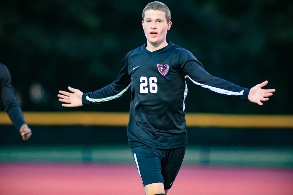 Soccer player number 26 in dark uniform celebrates with arms outstretched during match.