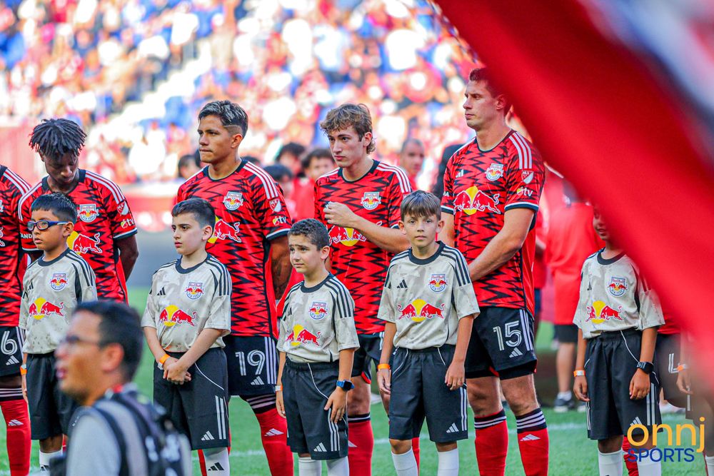 New York Red Bulls players line up with youth mascots during pre-match ceremony at stadium.