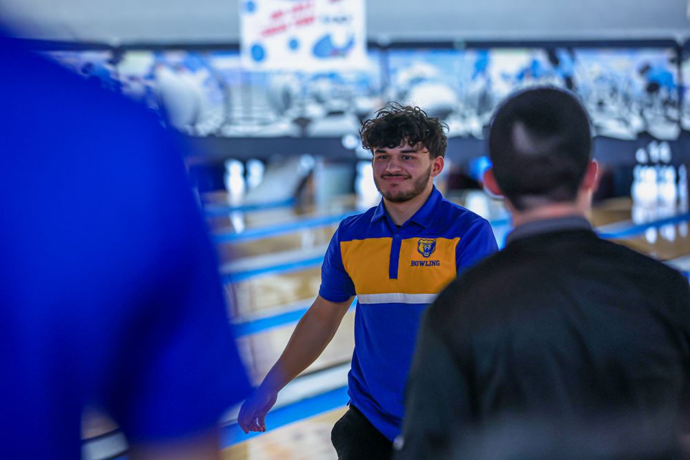 Young male bowler in blue and gold team jersey smiling at bowling alley during competition.