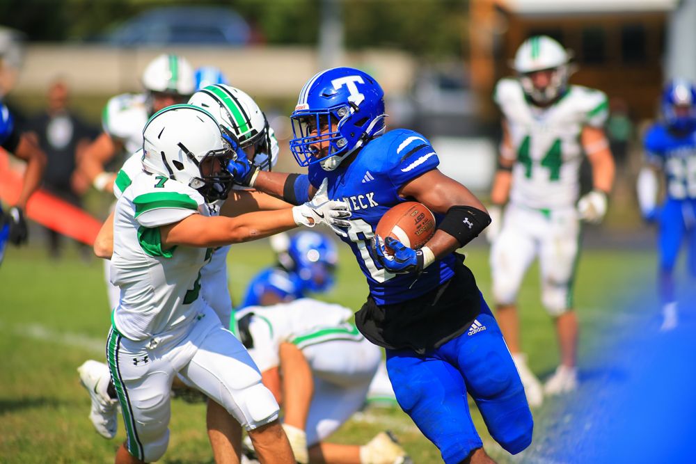 Blue jersey number 10 football player breaking tackle attempt during sunny outdoor game.