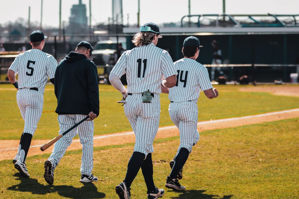Three baseball players in pinstripe uniforms walking together on field with coach during game.