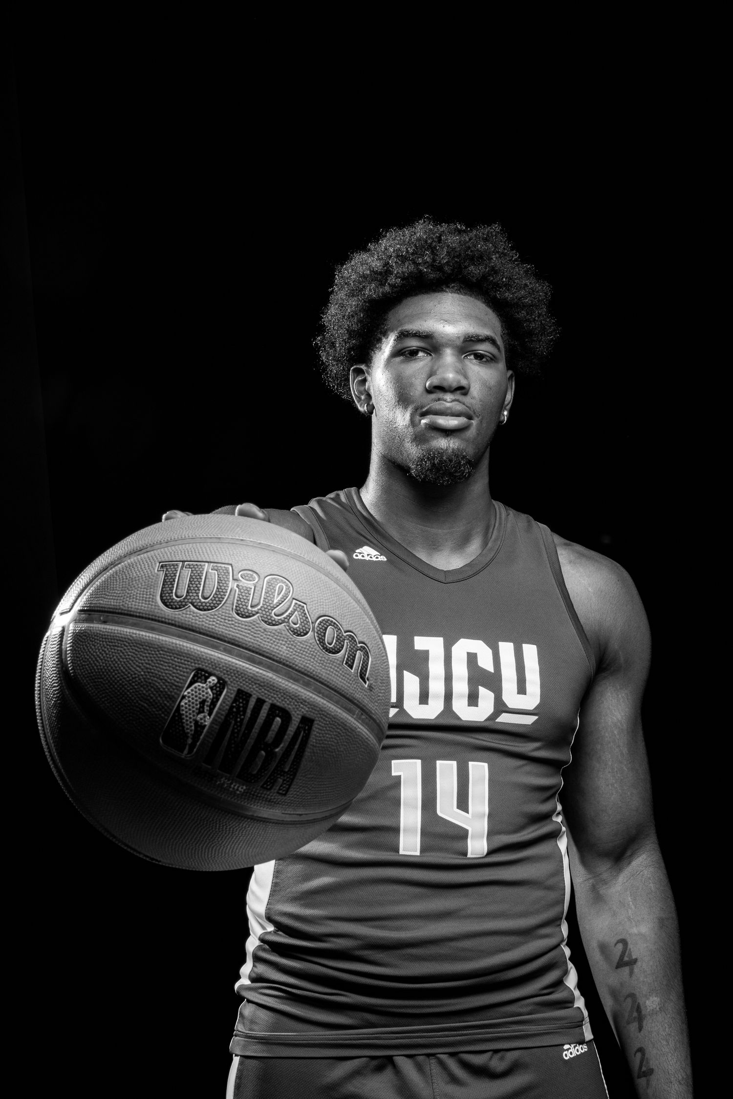 Black and white portrait of a NJCU basketball player wearing jersey number 14 holding a Wilson NBA basketball.