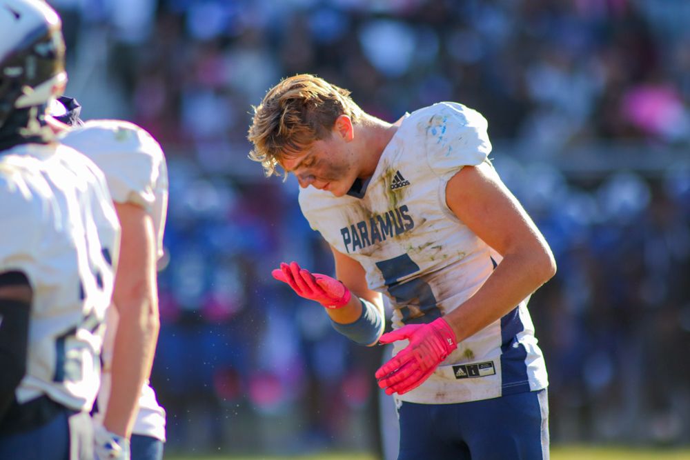 Paramus high school football player adjusting pink gloves during a sunny outdoor game.