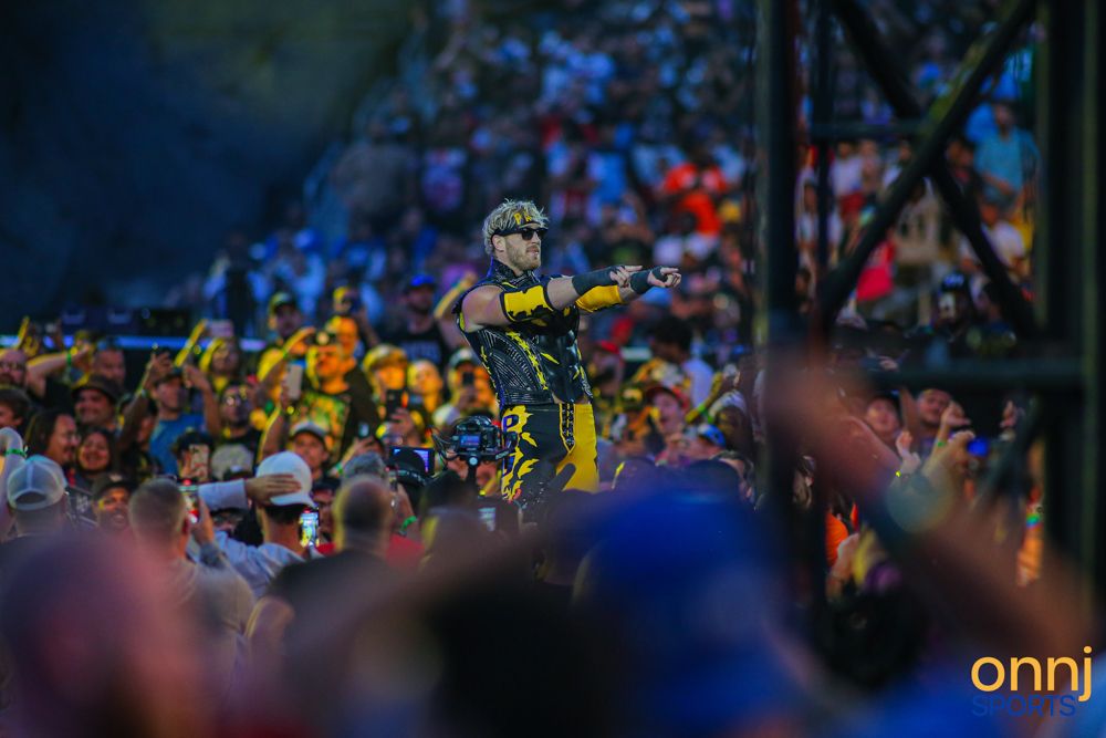 WWE performer in yellow and black gear stands among cheering fans at outdoor SummerSlam event.