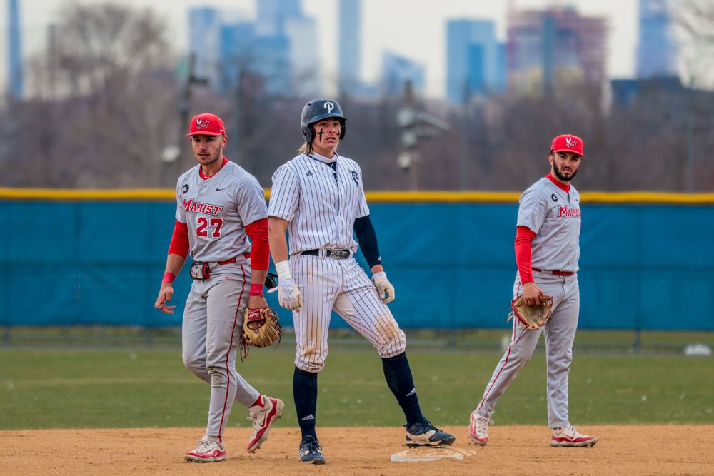 Baseball player stands on base between two red-uniformed fielders during spring game.