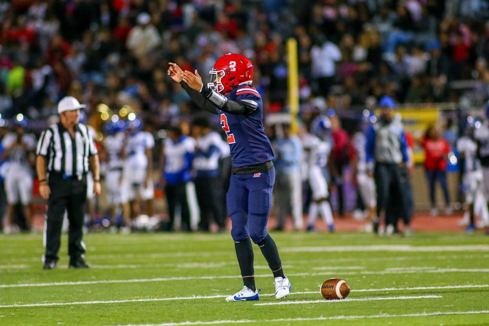 Football quarterback in red number 9 jersey signaling during night game under stadium lights.