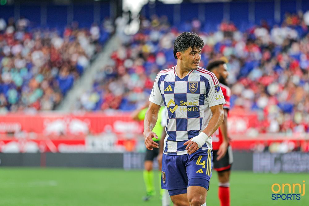 MLS soccer player in blue and yellow checkered jersey walks on field during a competitive match.